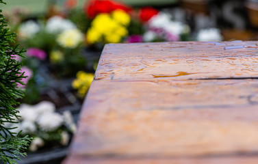 Krople deszczu na drewnianym stole. Ogrod przydomowy. Kolorowe kwiaty w tle.