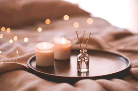 Aroma bamboo sticks in bottle with scented liquid with candles staying on wooden tray in bed closeup.