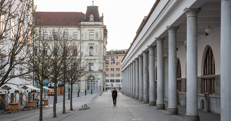 Rear view of unrecognizable woman walking in empty old medieval Ljubljana city center during corona virus pandemic. Almost no people outside on streets.