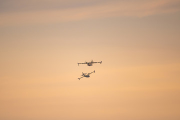 Two amphibious water bomber airplanes in flight at sunset, in France.