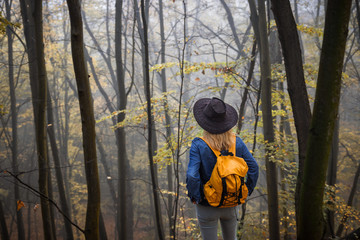 Obraz na płótnie Canvas Hiker with backpack and hat looking at fog in forest. Hiking in autumn nature 