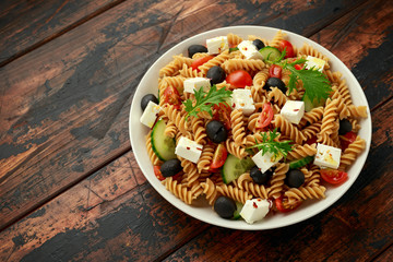 Pasta salad with tomato, black olives, cucumber and feta cheese on wooden table. healthy food.