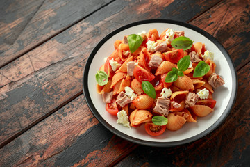 Conchiglie Tuna pasta with tomato sauce, feta cheese and basil on wooden table.