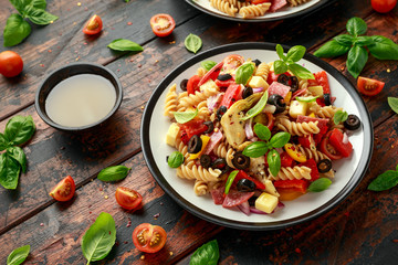 Antipasto salad with pasta, tomato, olives, red onion, bell pepper, salami, cheese, artichoke and basil.