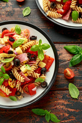 Antipasto salad with pasta, tomato, olives, red onion, bell pepper, salami, cheese, artichoke and basil.