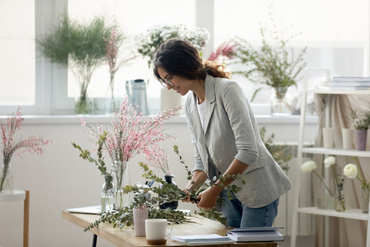 Side view smiling attractive female decorator arranging green plants leaves in wedding bouquet, making floral composition for event or house interior in modern creative office, gardening concept.