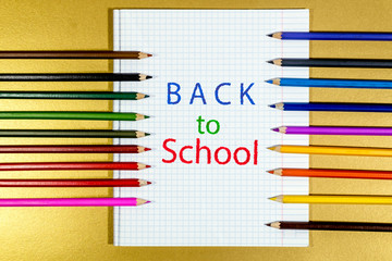 Colored pencils are lying on a white notebook sheet with the inscription back to school