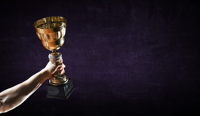 Hand holding up a gold trophy cup against dark background