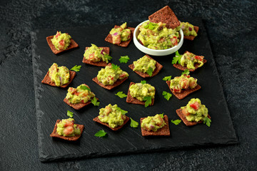 Avocado Guacamole with chipotle and poblano whole grain tortilla chips on rustic stone board