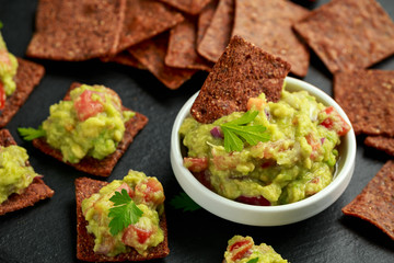 Avocado Guacamole with chipotle and poblano whole grain tortilla chips on rustic stone board