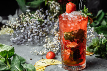 Strawberry Mojito. Cold summer mojito cocktail with strawberries, mint, lemon and ice in a glass on a table. on a dark background
