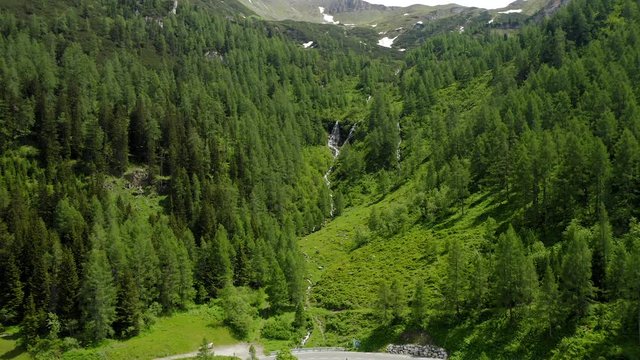 Aerial establishing footage of small waterfall and reveal in pinetree forest in summer season. Austria, Tyrol