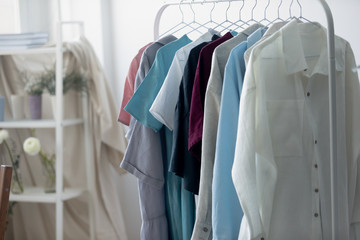 Close up new clothing collection hanging on rack in modern fashion atelier. Showroom interior with wardrobe high quality material clothes on hangers in creative office, dressmaking sewing concept.