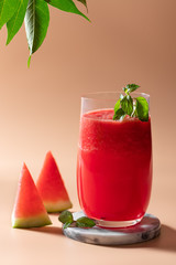 watermelon smoothie with mint in a glass on a beige background with green leaves. summer detox drinks concept. close-up. vertical image. copy space