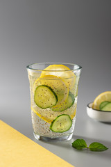 healthy chia water with cucumber and lemon in a glass. veggie detox drink. gray-yellow background. copy space. vertical image.