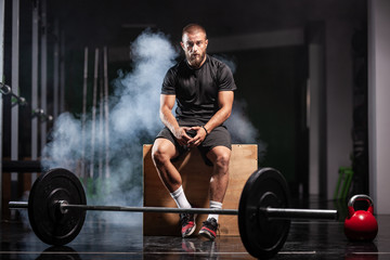 Muscular athlete with weightlifting equipment. Crossfit trainer in a fitness studio. Smoke background.