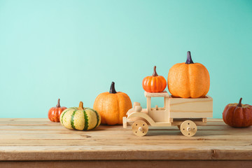Autumn season concept with toy truck and pumpkin decor on wooden table. Halloween or Thanksgiving greeting card.