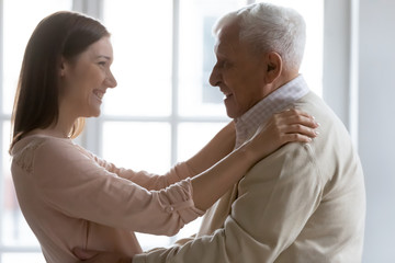 Obraz premium Side view happy positive elderly senior man greeting grown up child daughter at home. Smiling beautiful young woman glad to see older 70s father, enjoying visit at weekend free leisure time.
