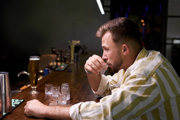 worried caucasian man sitting at bar with alcohol, young alcohol addict has problems in life