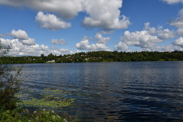 A picturesque view of a large river with green banks. Beautiful clouds are reflected in the water.