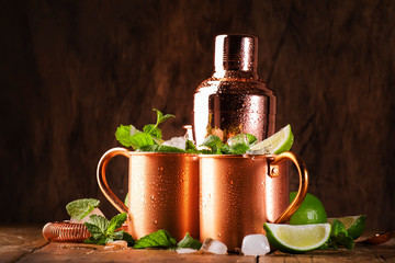 Moscow mule or mint julep cocktail in copper mug with lime, ginger beer, vodka and mint. Wooden table, copper bar tools,  copy space