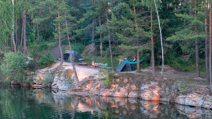 Camping on the lake. View of tourist tents located on the edge of a flooded granite quarry among pine trees