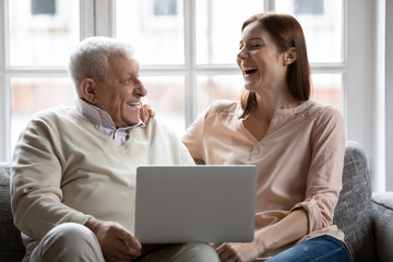 Overjoyed old 70s retired father sitting on couch, watching funny movie comedian film on computer with laughing grown up daughter, enjoying spending free weekend time together in living room.