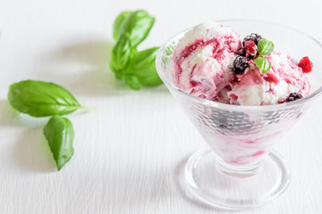 Fresh fruit ice cream in the glass bowl on the white table, green leaves of basil . Sweet dessert eating.