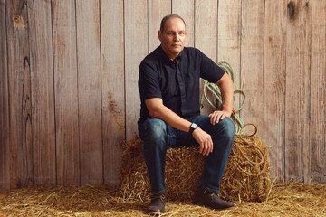 portrait of man resting on hay bale in barn - obrazy, fototapety, plakaty