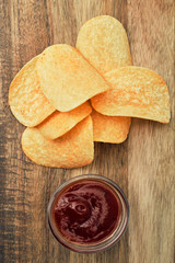 Potato chips on a wooden board with sauce. Snack, ready meal menu, junk food. Close up.