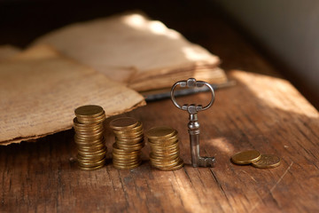 An old beautiful old key, a stack of gold coins, an old book. Business start-up, investment,...