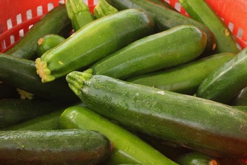 A basket of zucchini in a red basket set up at a farmer's market