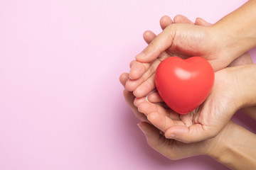 Hands holding a red heart on pink background, CSR or Corporate Social Responsibility, health care, family insurance, heart donate concept, world health day.