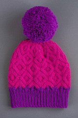 Beautiful two color handknitted hat with pompon on gray background. Top view