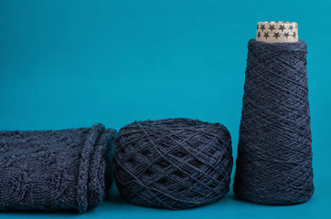 cone and ball of gray wool yarn, and part of knitted sweater on turquoise background