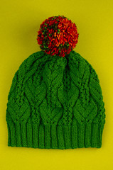 Beautiful kace handknitted hat with multicolored pompon on yellow background. Top view