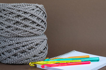 gray color with dots t-shirt yarn balls and colorfull crochet hooks on notebook on brown background. Craft, handmade, hobby concept.