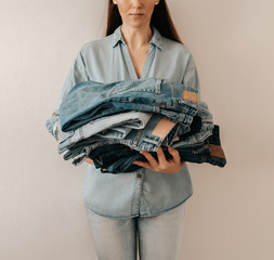 Unrecognizable woman holds stack of lot jeans pants on white background. Caucasian woman with long...
