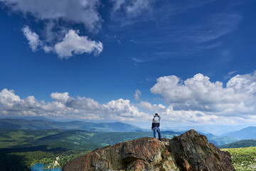 a man climber stands on the edge of a cliff and looks into the distance at the lake and mountains © Alexander