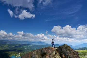 a man climber stands on the edge of a cliff and looks into the distance at the lake and mountains