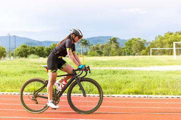 asian young woman athletes cycling on a race track intently and happily at outdoor sports field in bright day