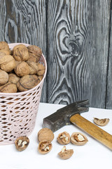 A basket with walnuts. Nearby is a hammer and chopped nuts. On a white surface.
