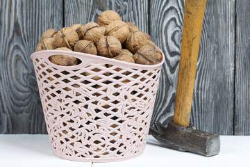 A basket with walnuts. There is a hammer nearby. Against the background of painted pine boards.