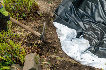 Pickaxe when loosening a wood root with the pond liner still to be laid in the background 