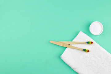 Bamboo toothbrushes, a white cotton towel and powder for brushing your teeth in bowl on  green backdrop.  No plastic, zero waste concept.