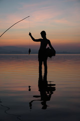 At lake side, asian fisherman sitting on boat while his son standing and  using fishing rod to catch fish at the sunrise