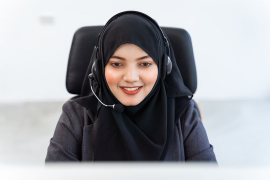 Arabian or Muslim woman works in a call center operator and customer service agent wearing microphone headsets working on computer, talking with customer for assisting with her service mind