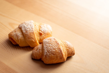 Two delicious croissants on wooden background with strong light coming from the corner