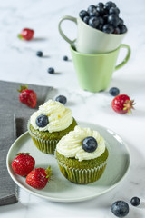 Yogurt and spinach muffins decorated with whipped cream with cups filled with blueberries in the background