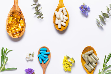 Flat lay overhead view of assortment of natural medical capsules for healthy lifestyle and beauty in the wooden spoons with flowers and  herbs. Health care concept. Immunity support mix.